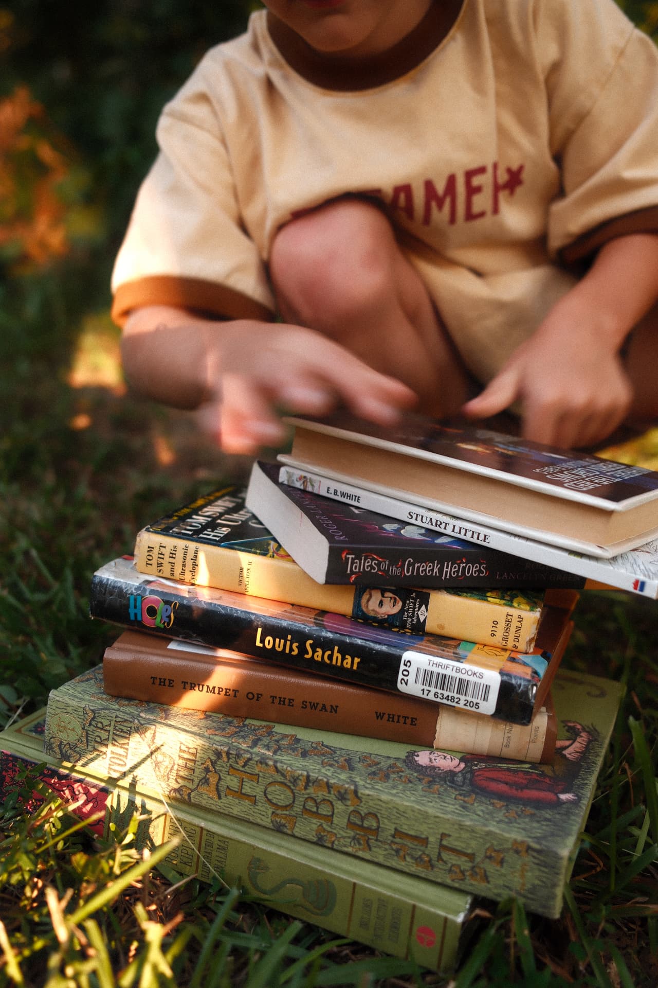 A child sitting in the grass with a stack of well-loved chapter books